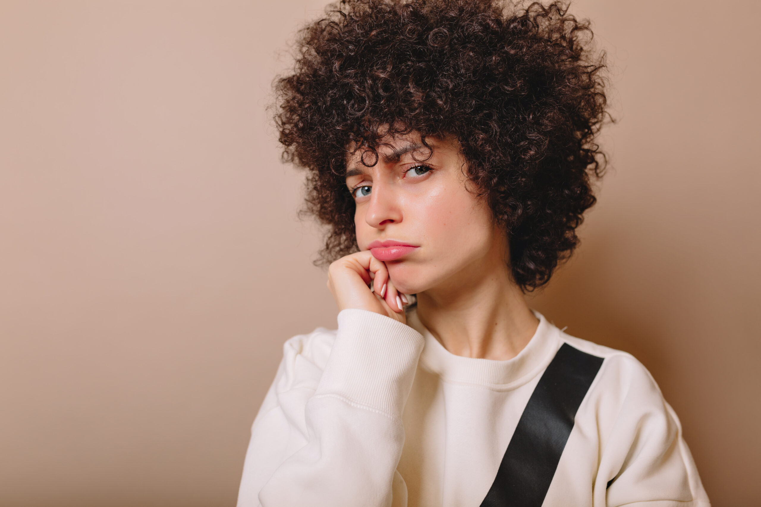 Funny girl with playfully puffed lips poses on beige background, funny emotions, isolated background